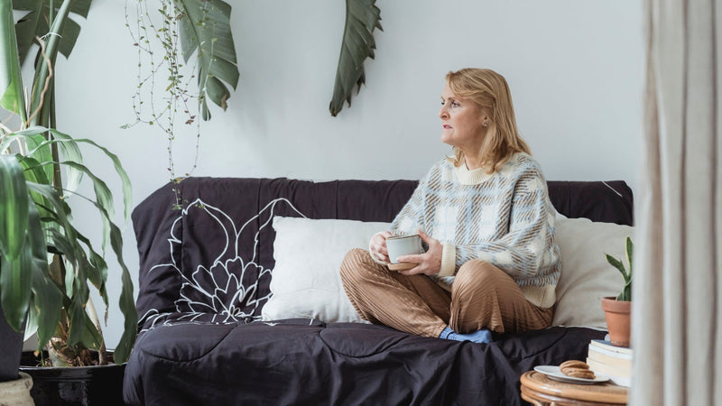 Woman in her fifties on a sofa holding a warm drink
